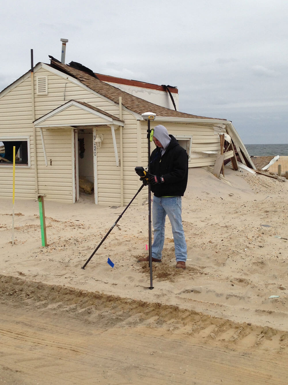 Surveyor measuring near damaged beach house.